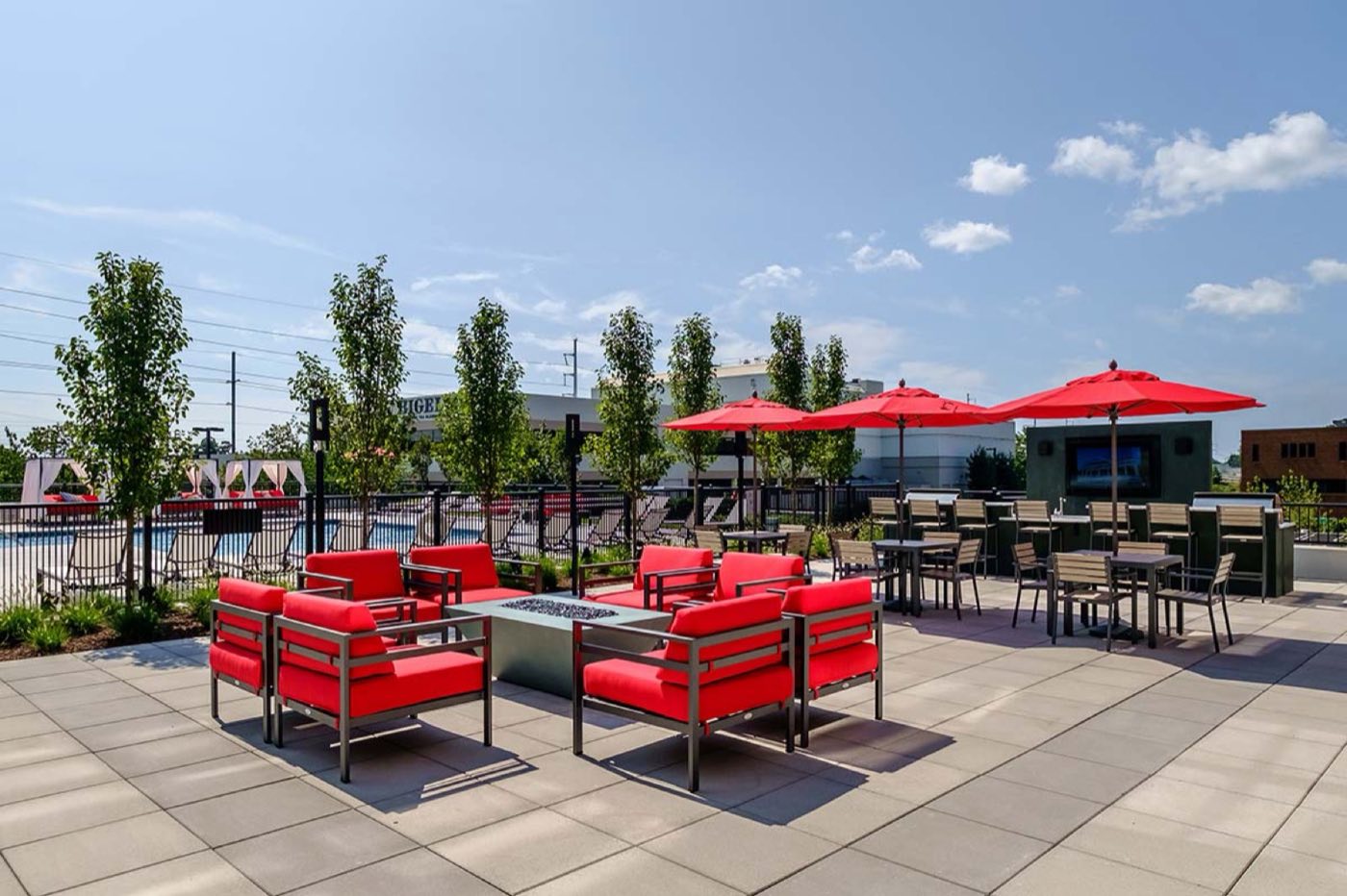 Red outdoor armchairs around a firepit with umbrellas and a television